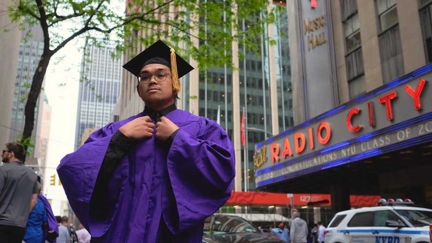 man wearing purple and black educational gown standing near building